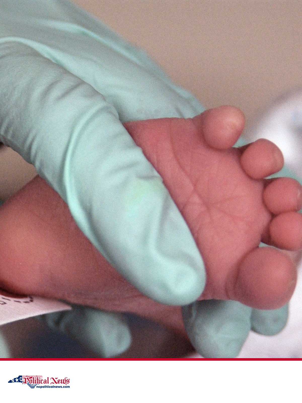A medical worker holds a newborn's foot during heel-prick blood collection for screening.